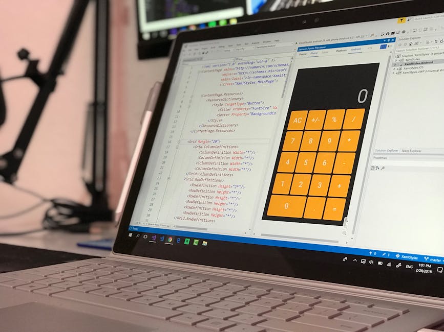 The image shows a close-up view of a laptop computer placed on a wooden desk, displaying lines of programming code on its screen with syntax highlighting in various colors, suggesting software develop